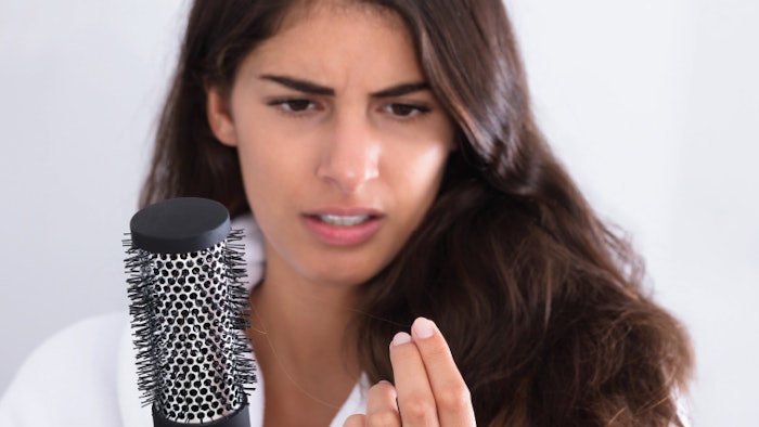 Woman looks at hair falling out of scalp while holding a brush in hand.