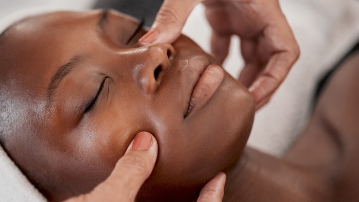 Black woman receiving a facial massage and spa treatment. Skincare, beauty and wellness spa with client feeling calm and zen