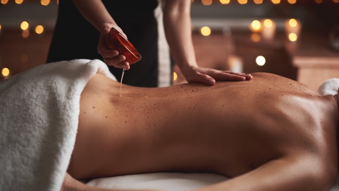 massage therapist pouring therapeutic oil onto client back for pain relief treatment