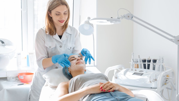 Woman professional doctor beautician applies a mask on a patient's face for skin care