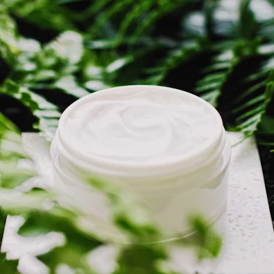 isolated-white-cream-jar-on-wet-white-surface-surrounded-by-greenery