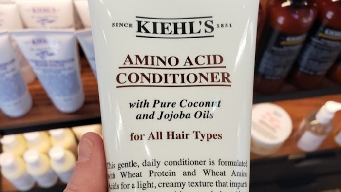 Kiehl's Amino Acid Conditioner held in store in hand background of other products on shelves