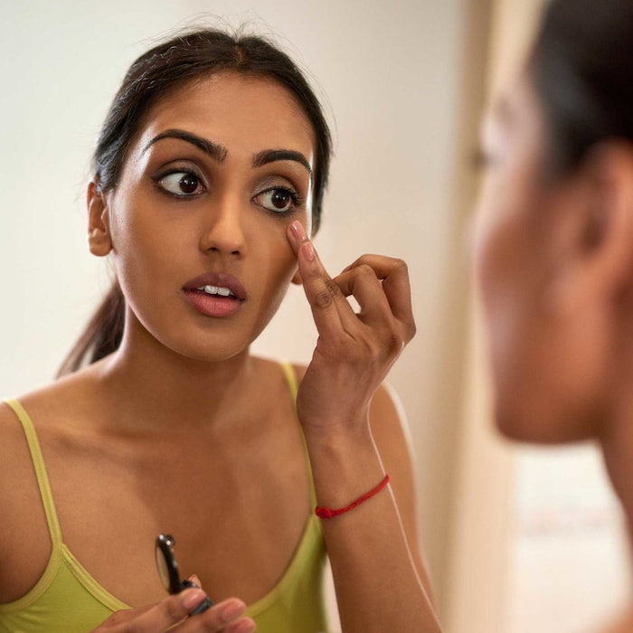 beautiful Indian woman applying eye makeup in mirror wearing green tank top