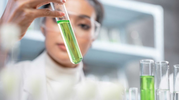 female chemist in lab blurred in background holding test tube with green liquid in it