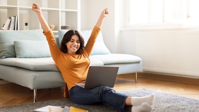 happy woman sitting on floor with laptop celebrating