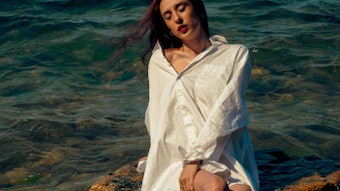 Woman seated on rock in ocean under the sun.