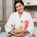 woman in robe in bathroom arms full of personal care bottles and products