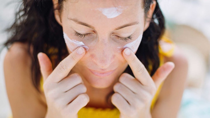 woman in yellow applying sunscreen to face with fingers head tipped down