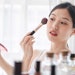 young beautiful Asian woman applying makeup in mirror products in foreground