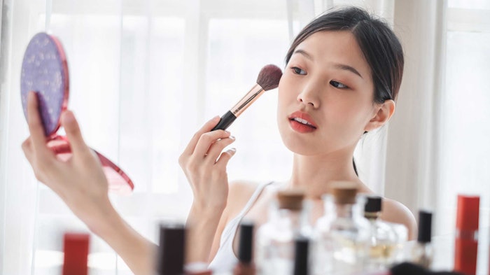 young beautiful Asian woman applying makeup in mirror products in foreground