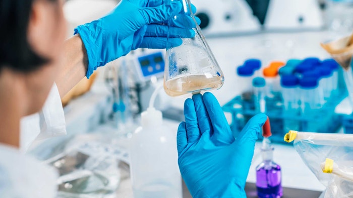chemist in lab examining flask fluid wearing blue rubber gloves