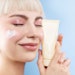 happy platinum blonde woman shiny skin holding product tube near and dear to her face