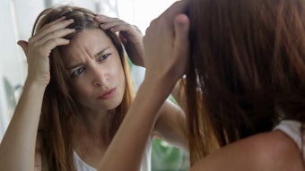 woman in mirror examining scalp stressed long red hair