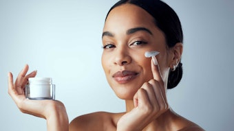 woman smart sassy holding jar of skin cream - hair pulled back - shoulders and up AdobeStock_595997467