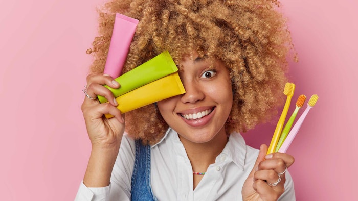 black woman holding toothbrushes toothpaste smiling bright colors