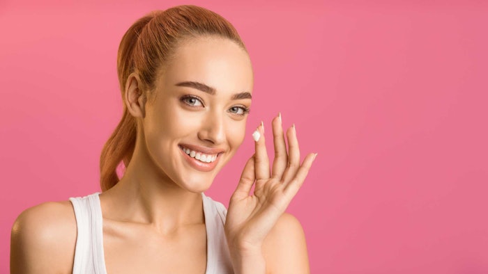 light skinned woman hair in ponytail pink background lotion dab on finger