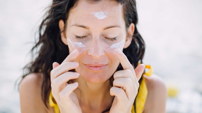 woman wearing yellow eyes closed applying sunscreen to face outdoors
