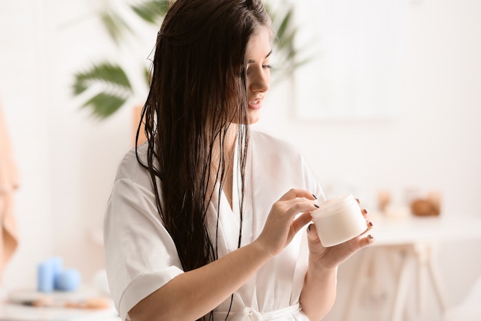 Woman with long brown hair holding a hair mask container.