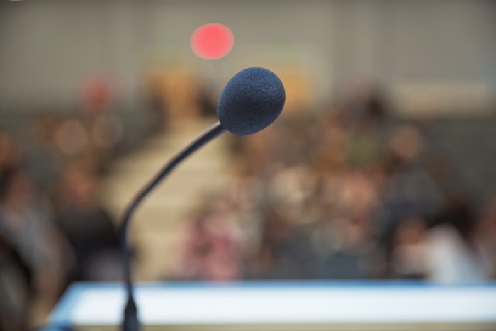 Point of View of view shot focused on a microphone on a podium with background blurred.