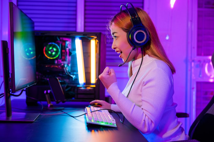 Woman with red hair and wearing headphones uses an online gaming platform on her desktop computer.,