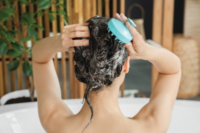 Woman massaging her scalp with a scalp brush in a bath tub.