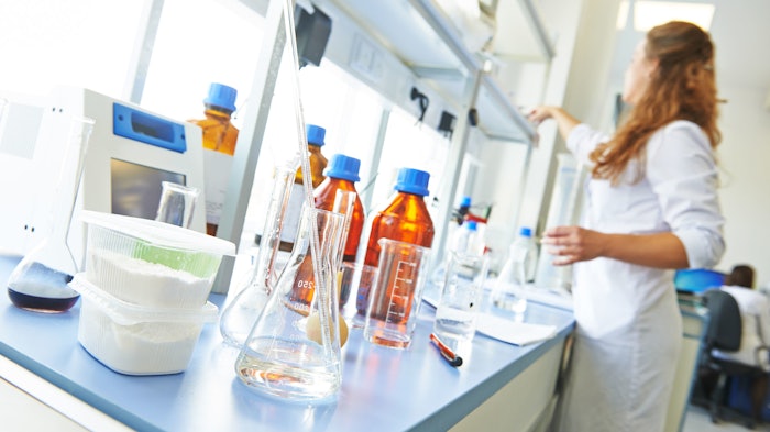 female chemist in lab benchtop and bottles of chemicals in foreground