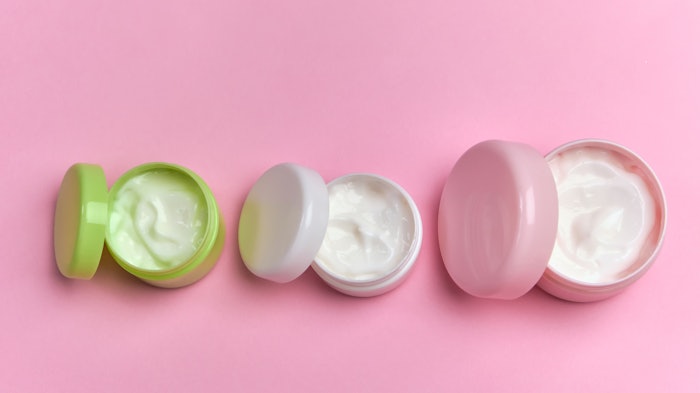 jars of cosmetic samples lids opened lined up pink background