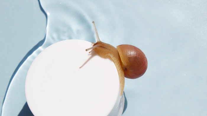 snail on skin cream jar slime background on blue