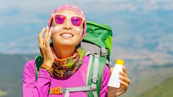 woman hiking mountains backpack using sunscreen