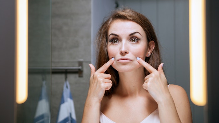 woman looking in mirror pulling frown lines up around mouth