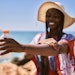 Beautiful Black Woman On Beach In Sunhat Using Sunscreen Blurred Back Focused Arm And Sunscreen adobe Stock 485102737