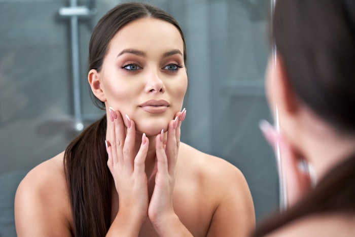 Woman Examining Her Face In The Mirror Adobe Stock 409806951