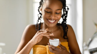 Beautiful Black Woman In Orange Towel Dipping Finger Into White Face Cream Jar Adobe Stock 578686567 (1)