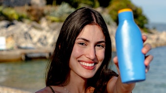 Beautiful Woman On European Beach Holding Up Blue Bottle Of Sunscreen Adobe Stock 1459804559