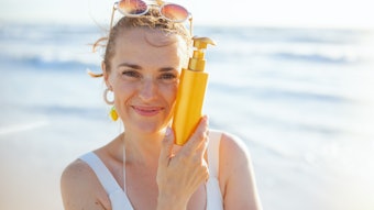 Woman On Beach Holding Sunscreen Bottle Smiling Adobe Stock 561891115 (1)