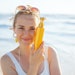 Woman On Beach Holding Sunscreen Bottle Smiling Adobe Stock 561891115 (1)
