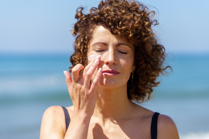 Woman Outside At Beach In Sun Applying Sunscreen To Face Adobe Stock 612484375
