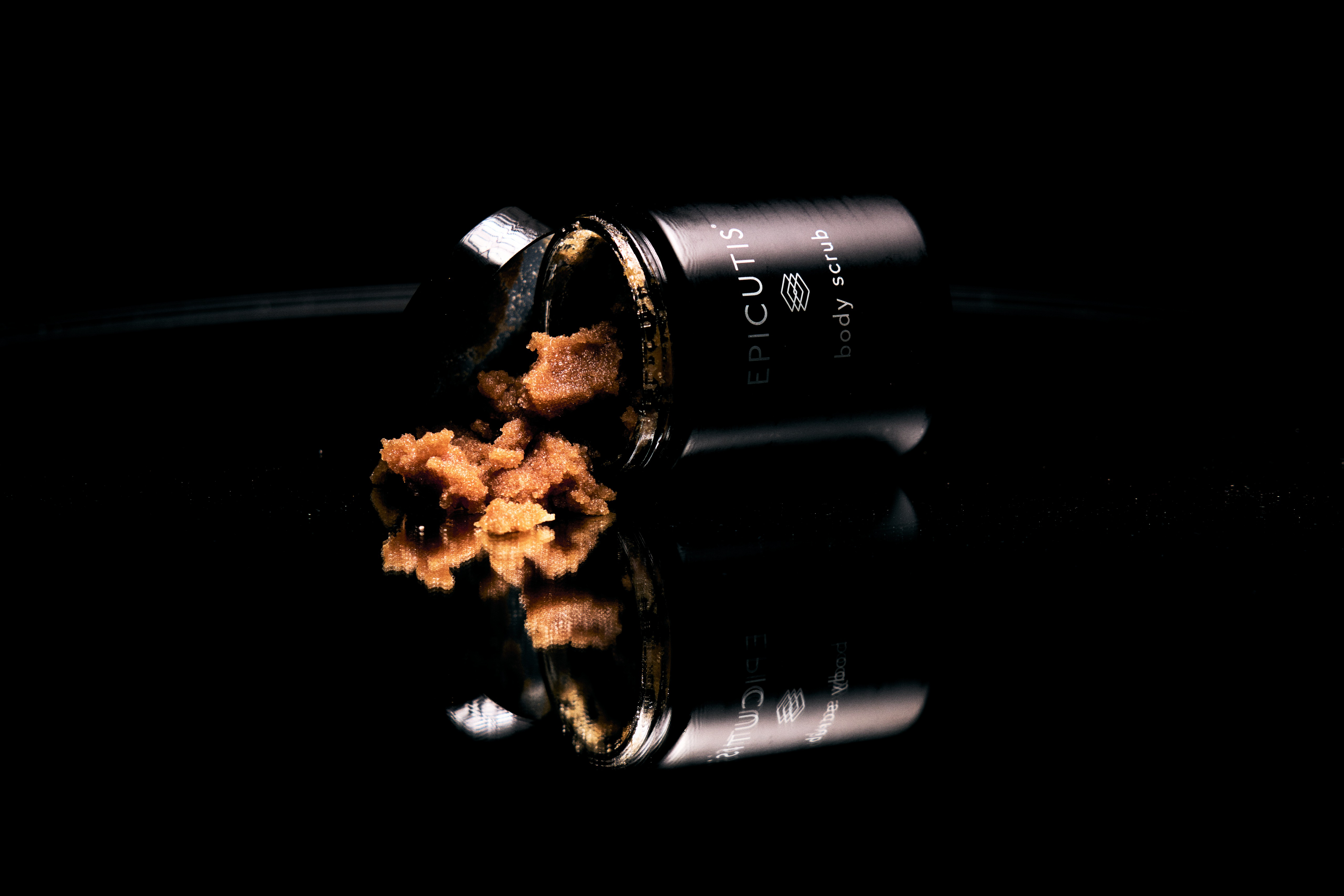 Black cosmetic powder container with bronze powder spilling out on dark background