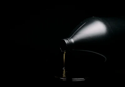 Bottle pouring golden liquid into glass on dark background