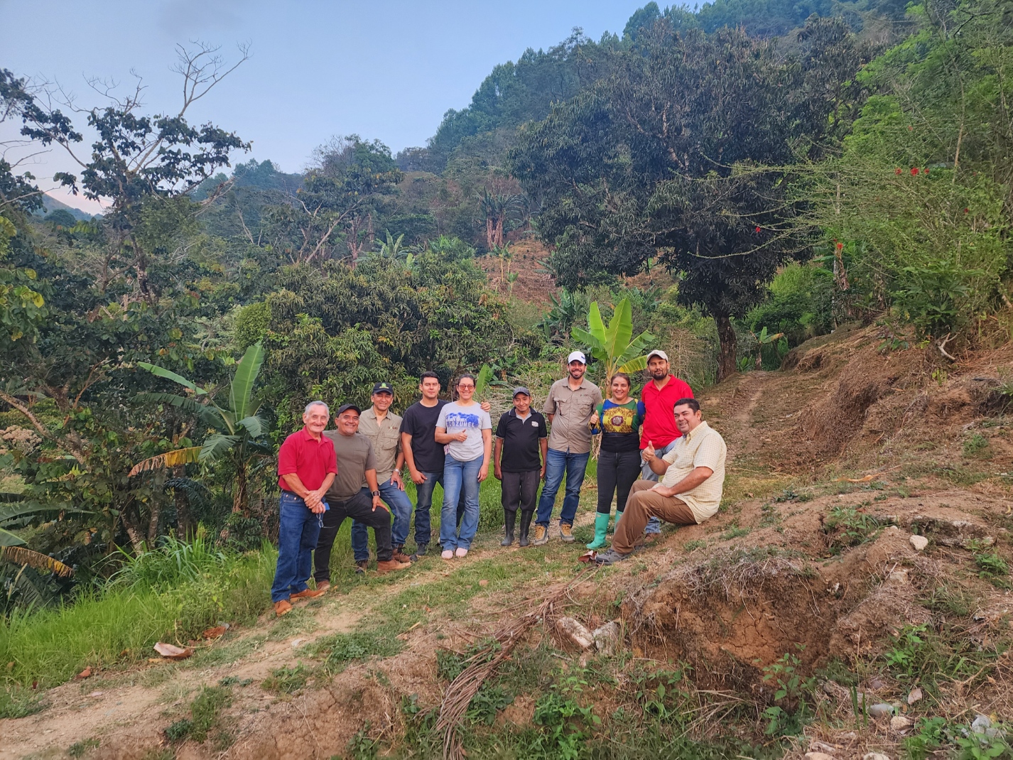 Group of people standing together on cleared land with forested mountains in the background