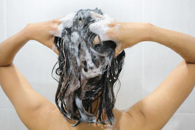 Person lathering hair with shampoo and soap during shower