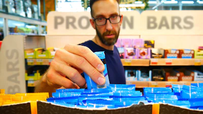 Man examining blue protein bars at retail display with shelving in background
