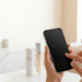Person holding smartphone with black screen in modern bathroom with beauty products on counter