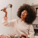 Woman with curly hair laughing while holding a whisk with chocolate batter dripping in a bright kitchen