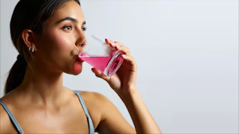 Young woman drinking pink beverage from striped cup against neutral background