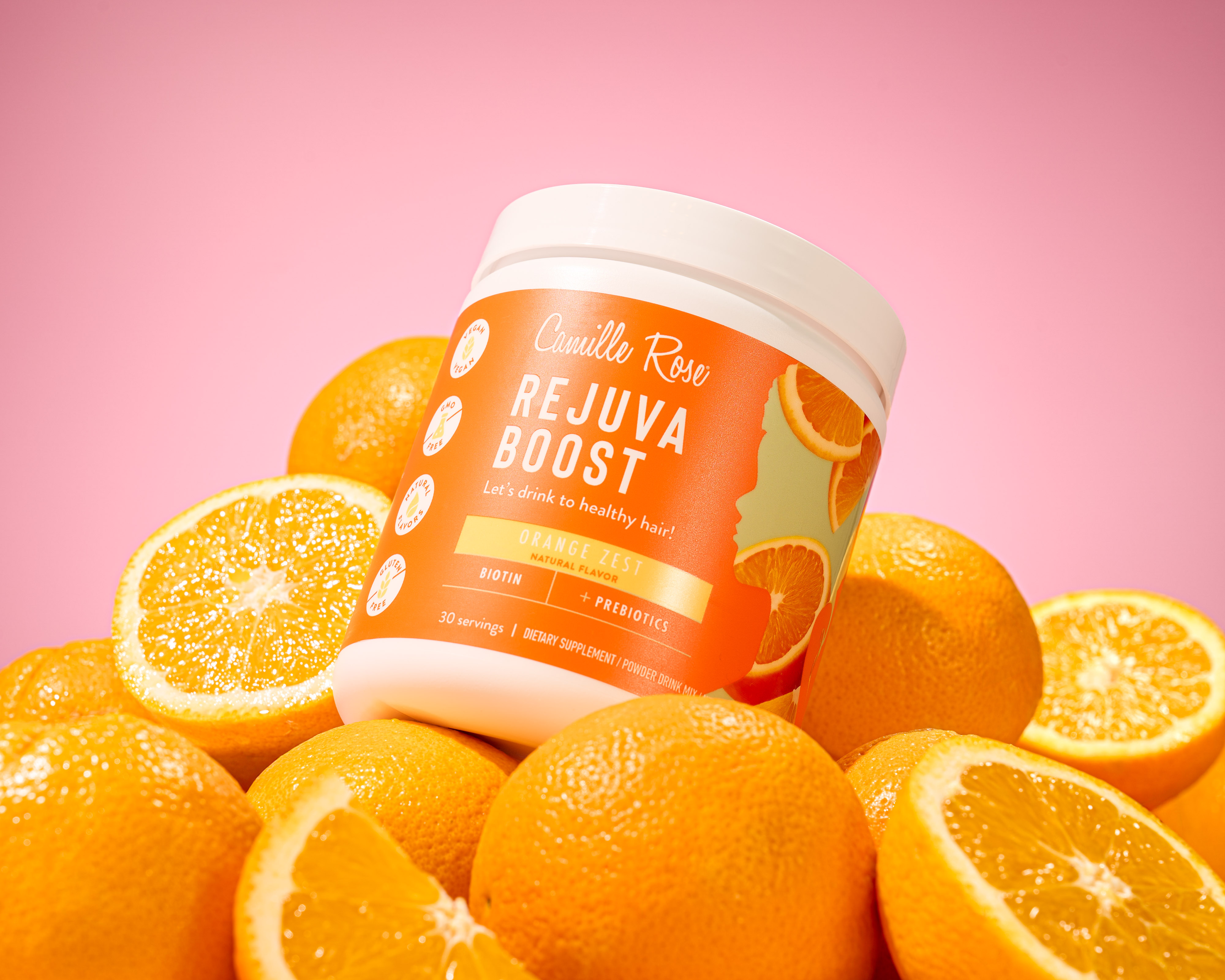 Camilla Raw Rejuva Boost hair supplement jar surrounded by fresh oranges on pink background