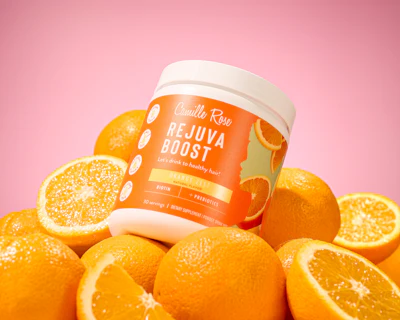 Camilla Raw Rejuva Boost hair supplement jar surrounded by fresh oranges on pink background