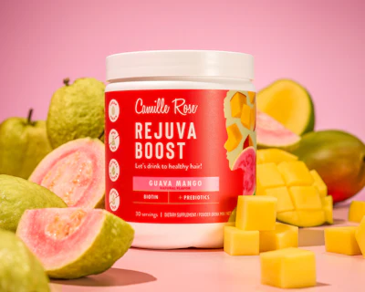Camille Rose Rejuva Boost hair supplement jar with guava and mango fruits on pink background