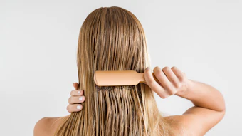 Woman brushing long brown hair with wooden paddle brush from behind