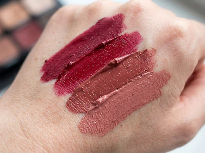 Four swatches of burgundy and nude lipstick shades displayed on skin for color comparison